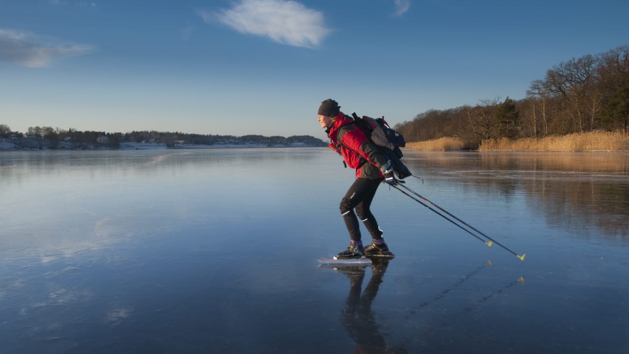 En man åker långfärdsskridskor på en sjö, det är en solig vinterdag.