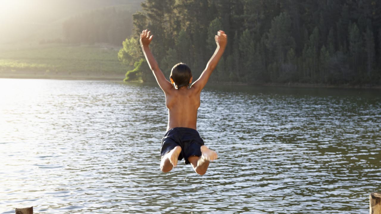 Pojke hoppar i sjön från brygga