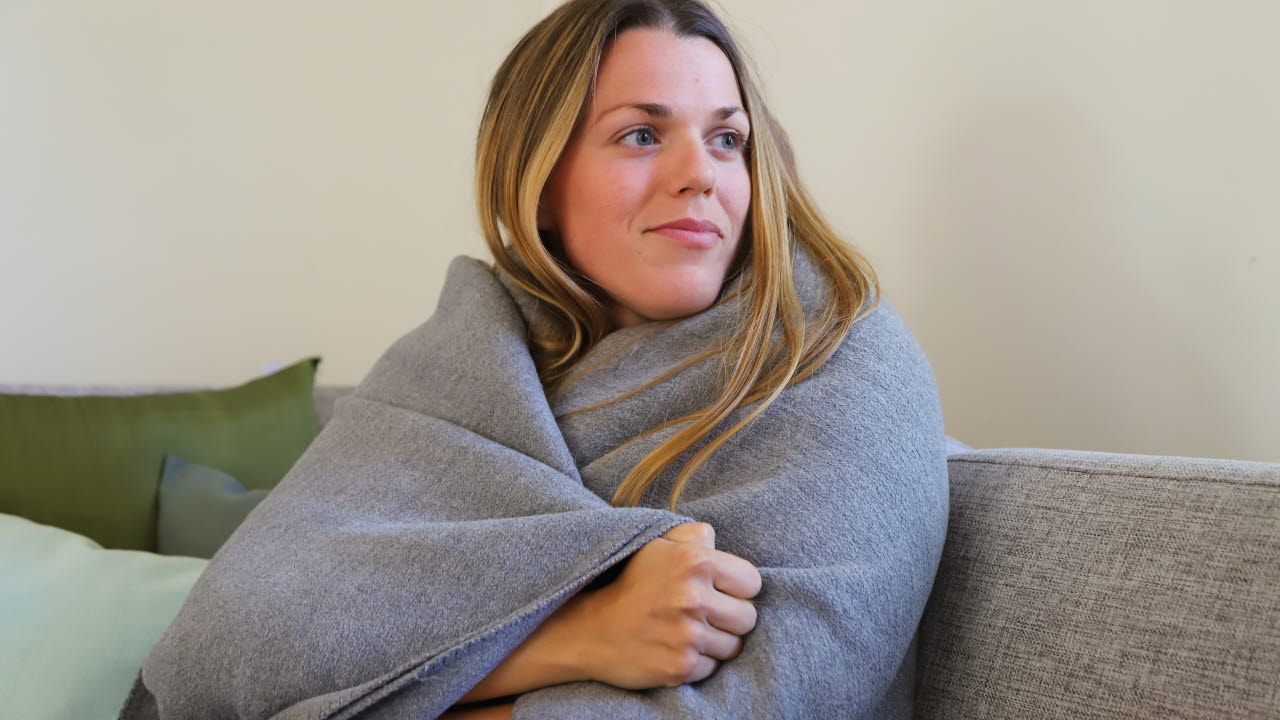 Kvinna som sitter i en soffa med en filt omkring sig
