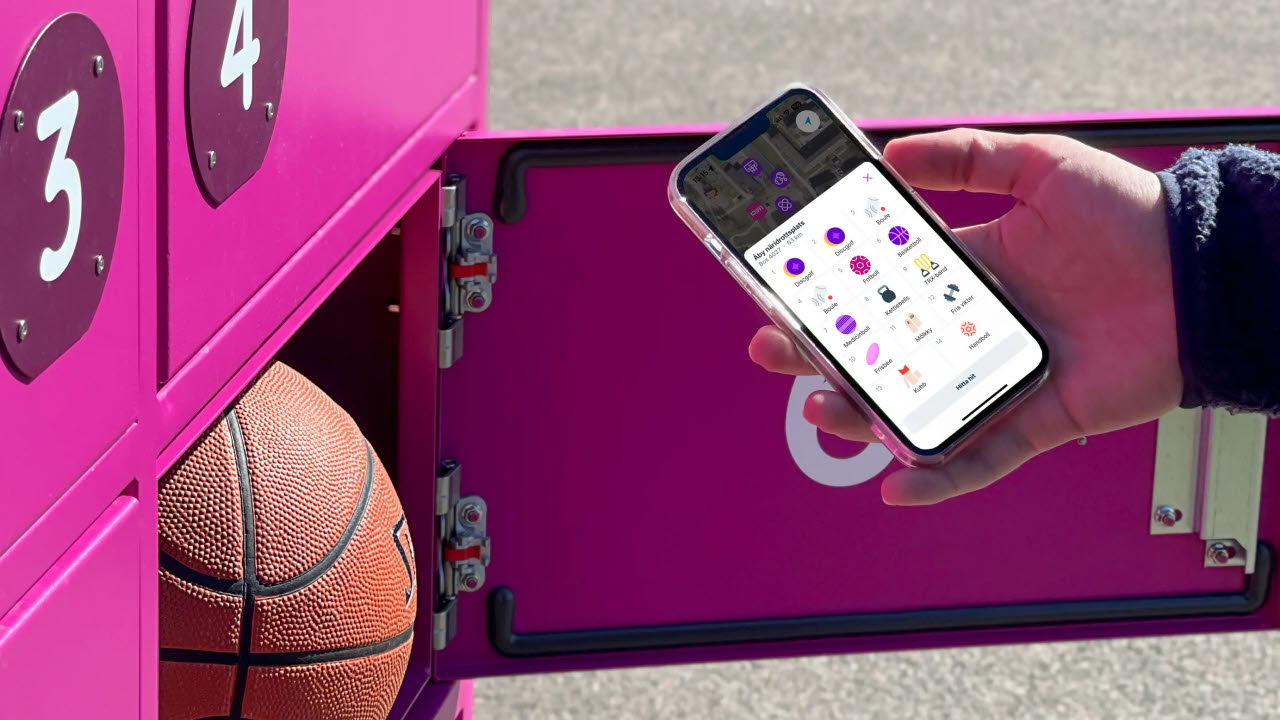 En hand som håller i en mobiltelefon med Piffl-appen öppen framför ett rosa Piffl-skåp där en av lådorna är öppen där finns en basketboll.