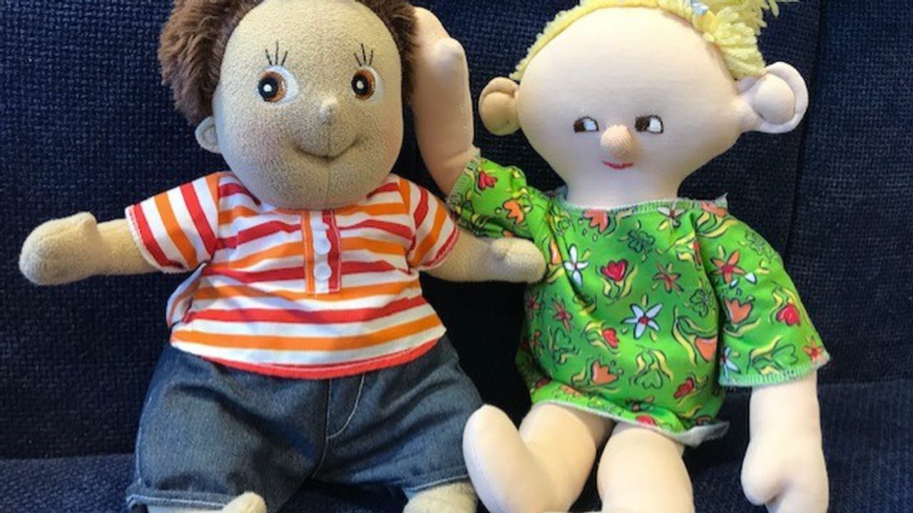 Två mjuka dockor klädda i färgrika kläder, som sitter bredvid varandra.