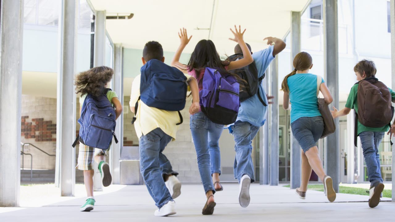 Barn med ryggsäckar springer utanför en skola