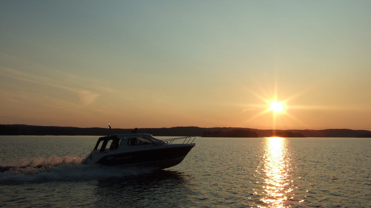 En fritidsbåt kör över en sjö. Solen håller på att gå ned vid horisonten.