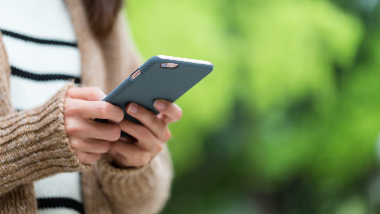 En kvinna skriver på sin smartphone, hon befinner sig utomhus.