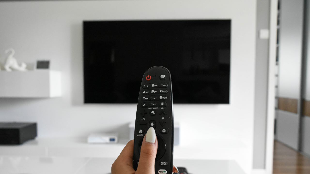 En hand håller i en fjärrkontroll till en tv