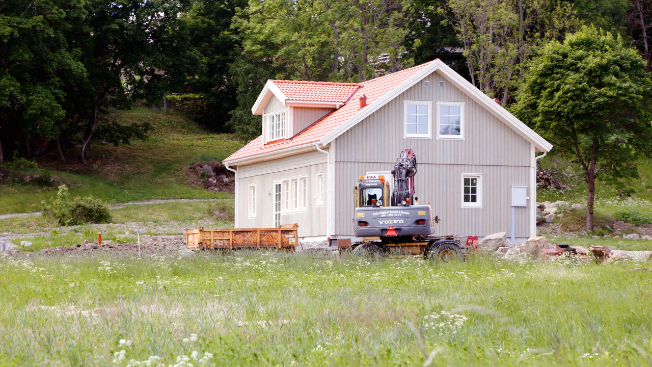 En grävmaskin vid gaveln på en modern nybyggd villa med härlig natur runtom.