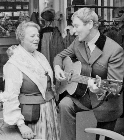 Svartvitt fotografi på Clara Johansson när hon och Tore Skogman sjunger och Tore och spelar på akustiskt gitarr. Bilden är tagen inifrån Clara's Konditori.