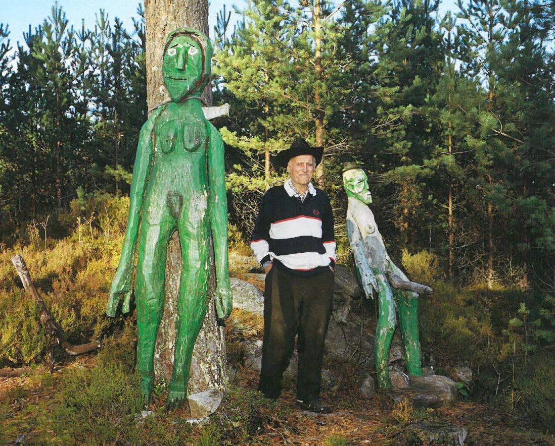Linder Eriksson står mellan två av sina skulpturer i en skog.