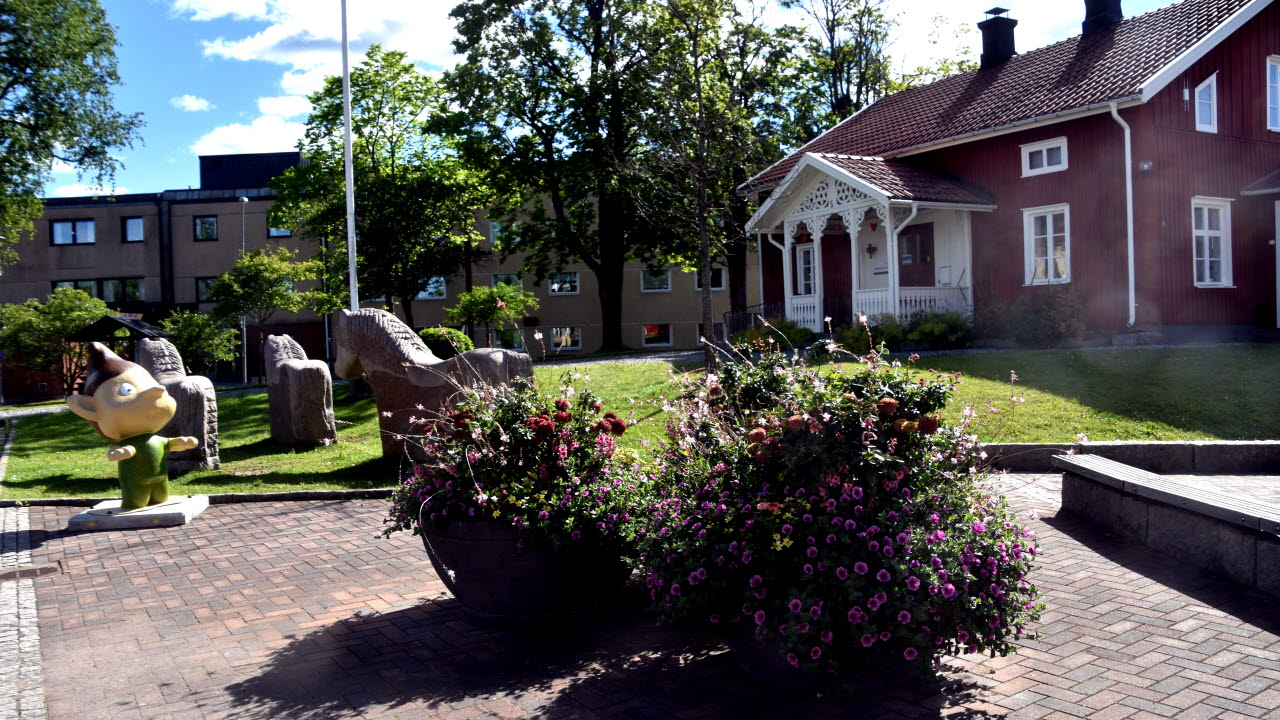 Rött hus på torget i Årjäng, stenhästar och färgglada blomkrukor