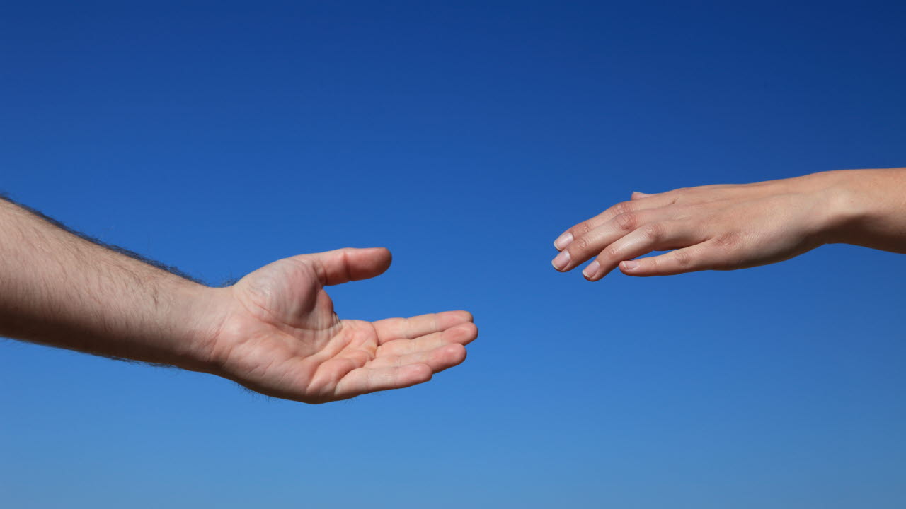 Två olika händer som sträcker sig emot varandra mot en blå bakgrund.