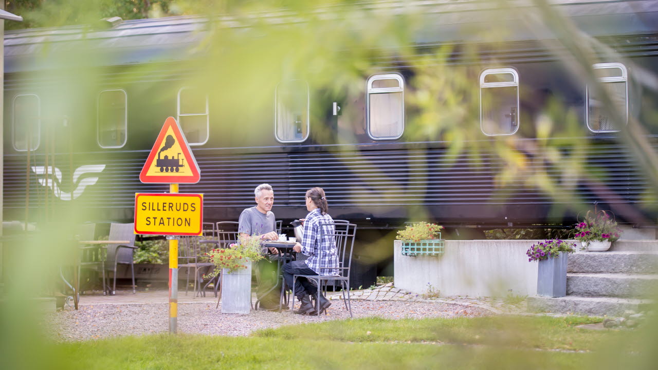 Två personer sitter och fikar på en perrong. På perrongen står det ett tåg