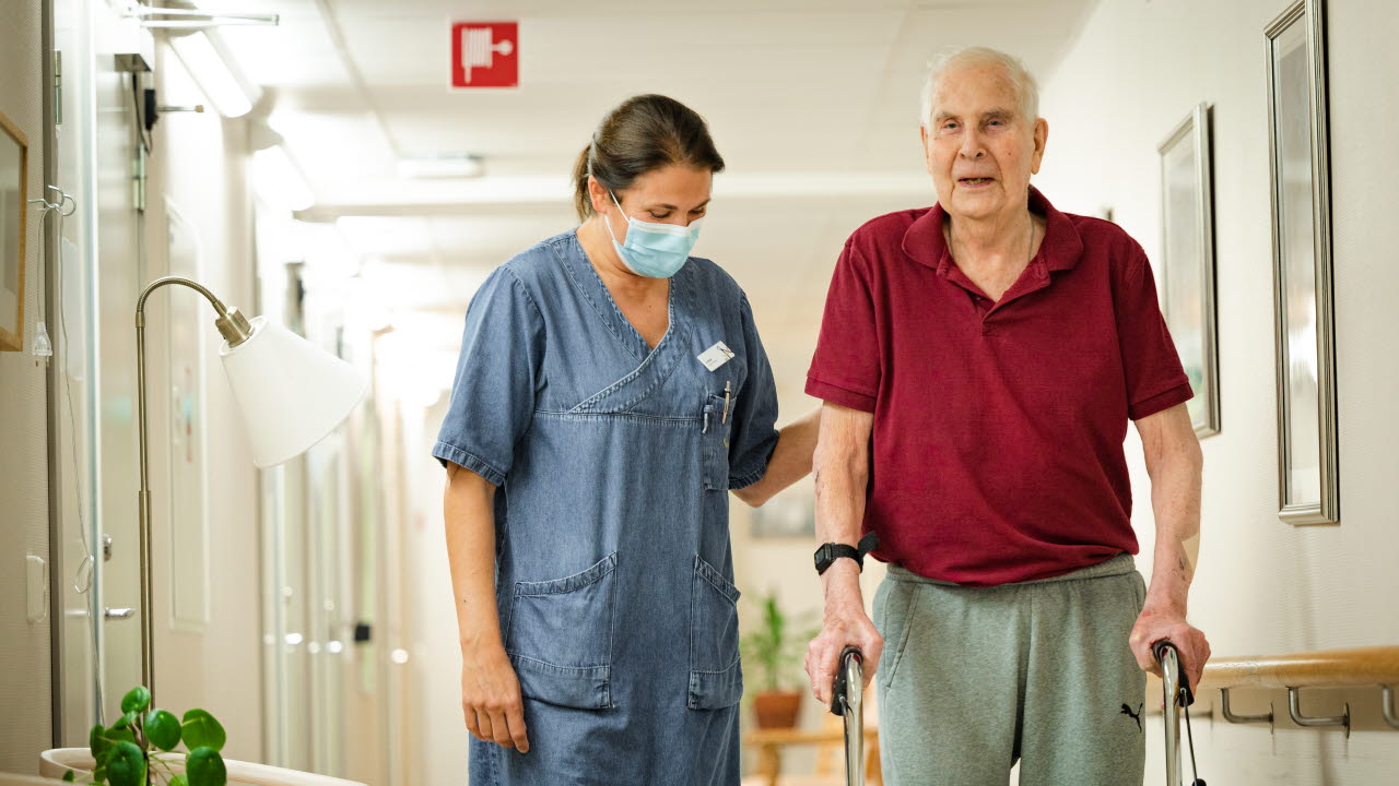 Undersköterska promenerar med brukare i korridoren på äldreboendet