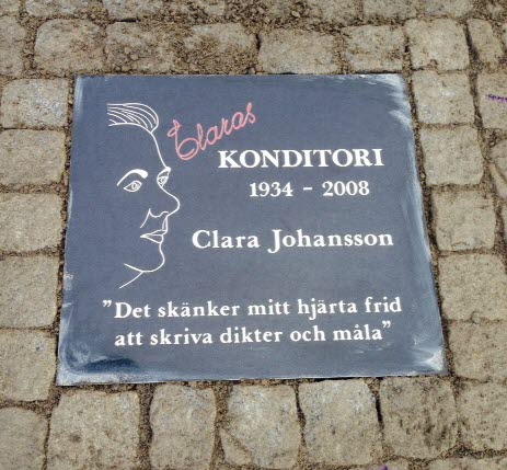 Minnessten infälld i kullerstenarna. Texten lyder: Claras Konditori 1934 till 2008 Clara Johansson. Ett citat från Clara står längst ned på stenen, det lyder: "Det skänker mitt hjärta frid att skriva dikter och måla."