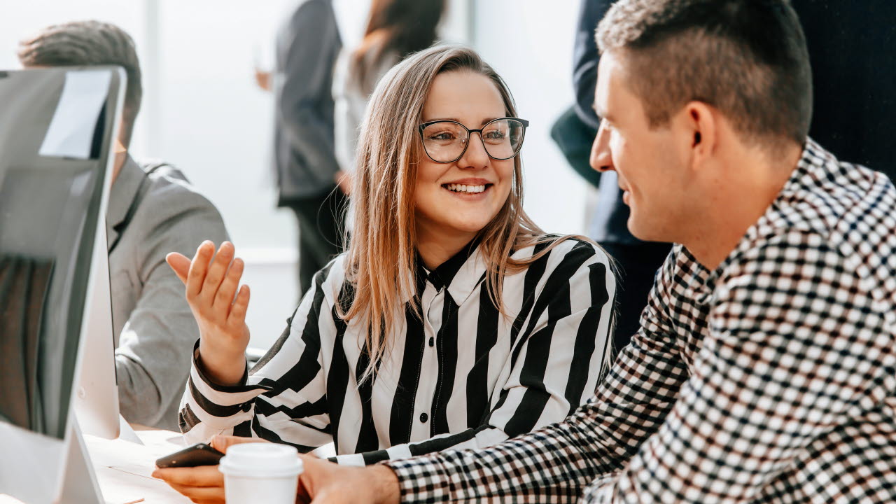 En kvinna och en man sitter vid ett skrivbord framför en dataskärm och samtalar